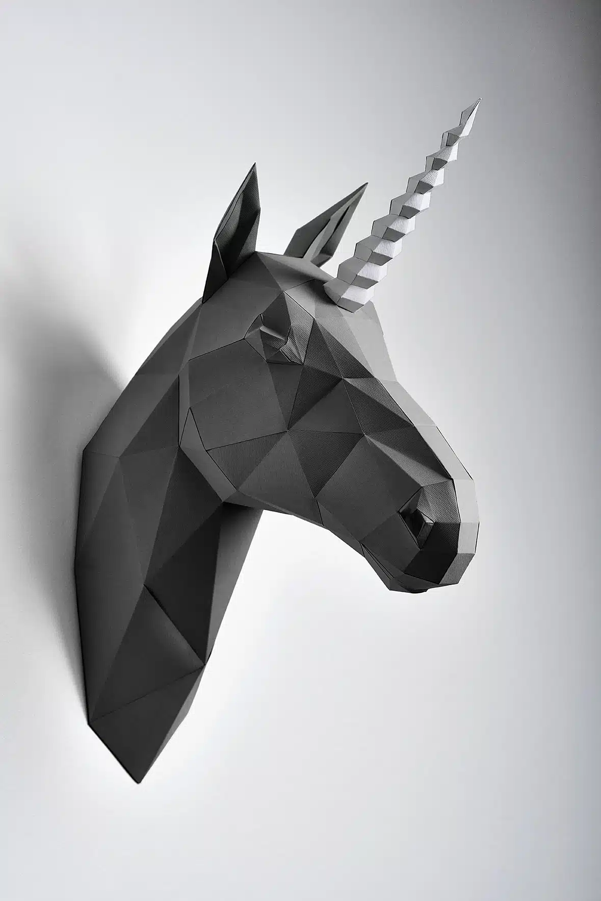 Escultura de un unicornio negro de papel sobre fondo gris claro